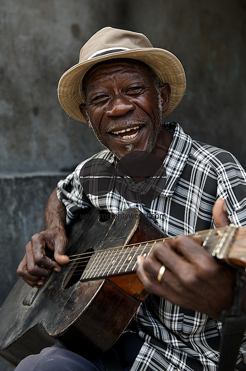 Haiti old man playing guitar and singing on the street.