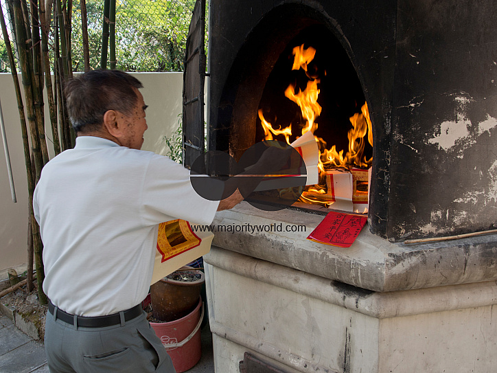 Elderly man burning paper money at a temple on the eve of Chinese New Year in Singapore