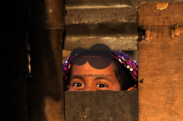 A young girl peeps through a window. Bangladesh