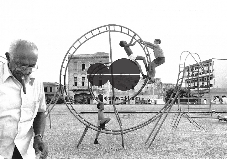 CUBA.ELDERLY MAN WITH CIGAR LOOKING AFTER HIS GRANDCHILDREN PLAYING IN A PARK IN HAVANA.1991