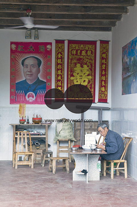 CHINA Elderly man with Mao poster on wall in a traditional Hakka house in a village  in Fujian province.