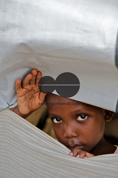 Young Haiti girl looks out from between sheets.