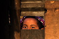 A young girl peeps through a window. Bangladesh