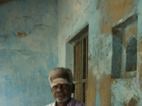 India. Man seated at entrance to his house.